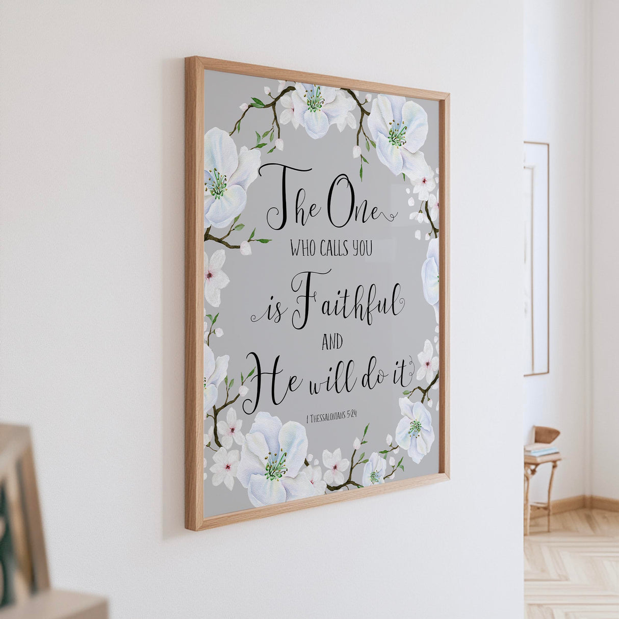 Grey and white floral wall art featuring 1 Thessalonians 5:24 Bible verse, "The one who calls you is faithful."