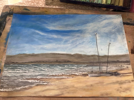 ‘Sandbanks Beach’ captures golden sands, a resting boat, and blue coastal skies in soft pastels.