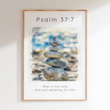 Psalm 37:7 - Rest In The Lord scripture wall art print with watercolour stacked pebbles and soft blue bokeh background.